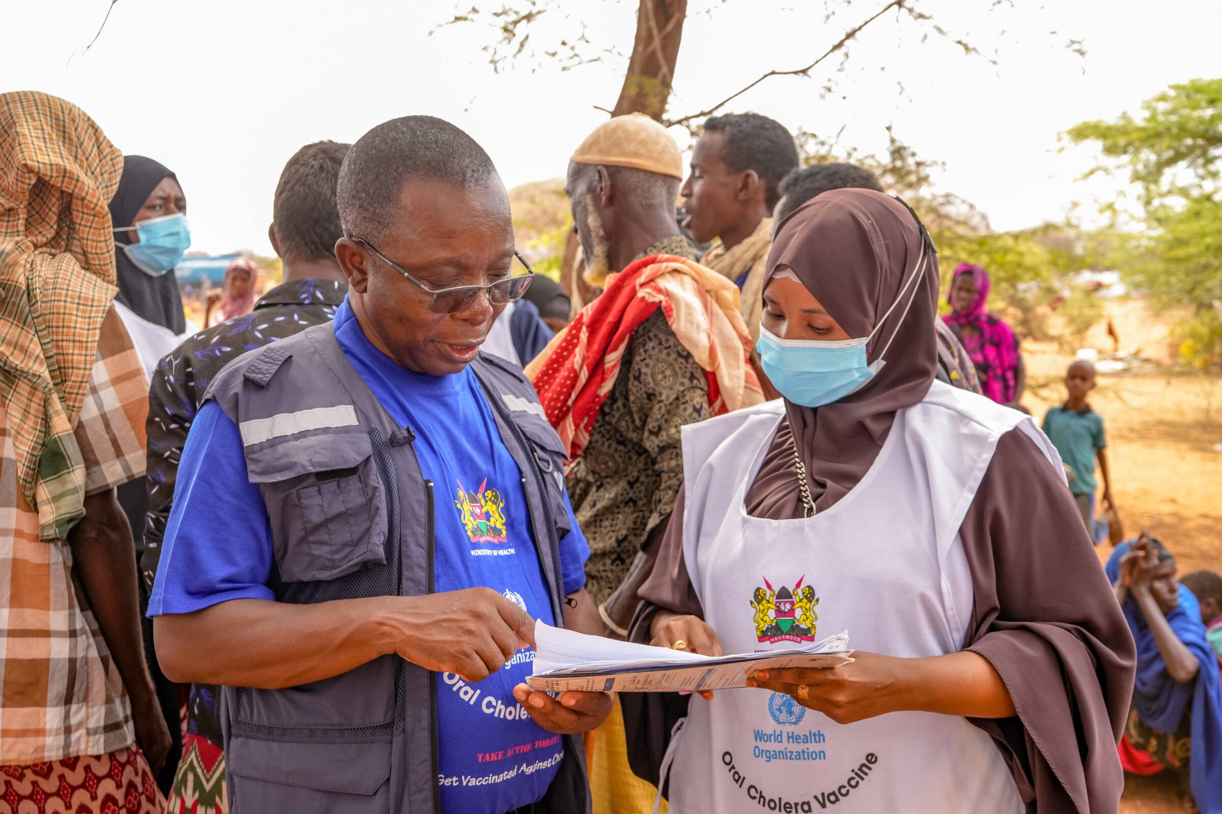 A WHO officer is looking through vaccine records during a vaccination campaign in an outdoor setting.