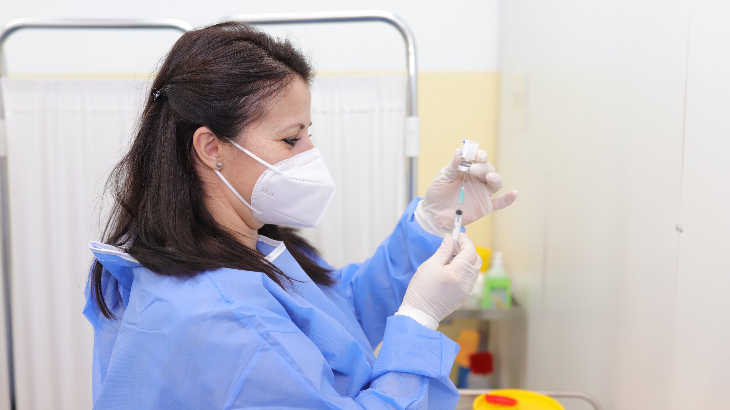 A female doctor or nurse in protective clothing extracts vaccine into syringe.